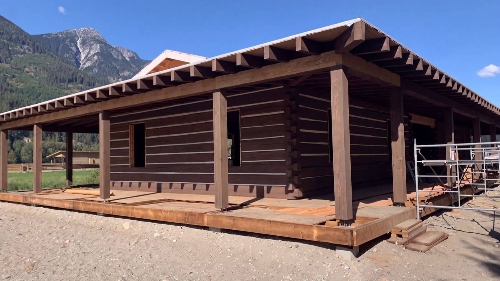 A log home in Pemberton Meadows, BC, freshly stained and chinked under a wraparound porch, with mountains behind
