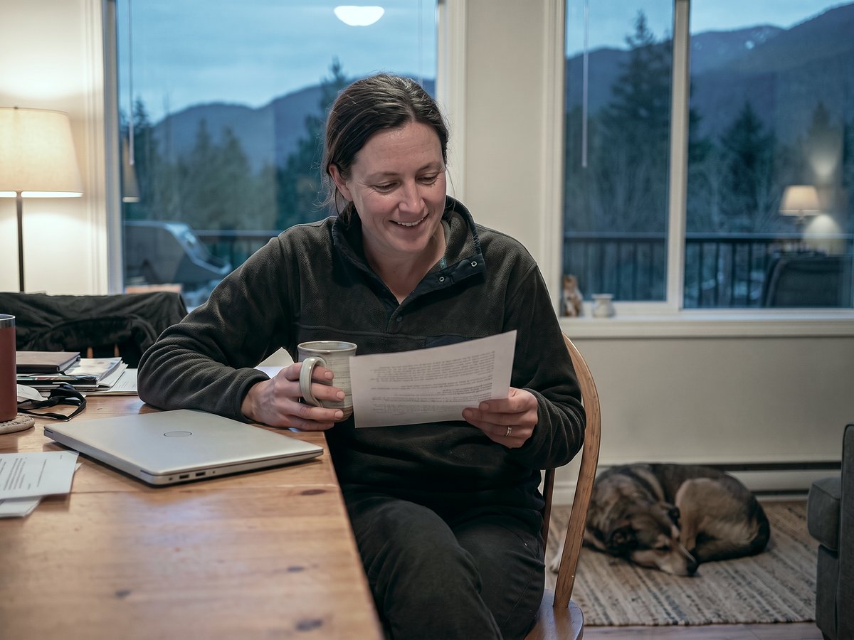 Cleaning company owner smiling over a one-page monthly summary at her kitchen table in the evening, laptop closed, dog asleep nearby