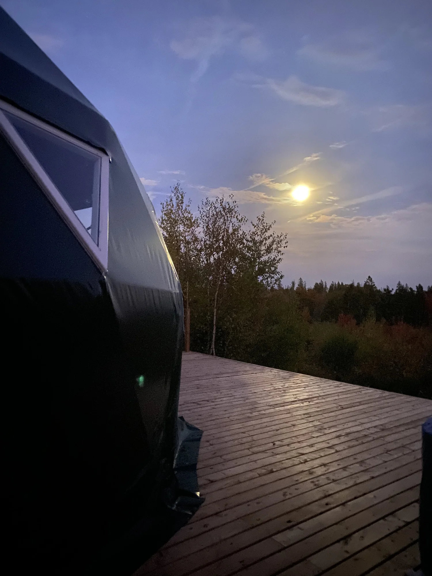 A geodesic glamping dome at PEI Centerline Escapes at dusk, with a private deck and the moon rising over the Prince Edward Island forest